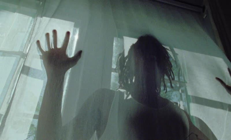 A man stands behind drapes in a home and slaps his hands against the drapes like he is trapped