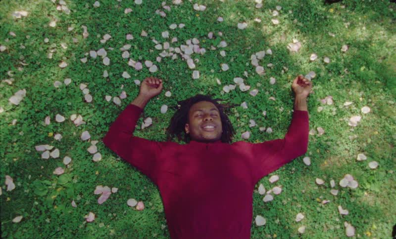 A man is lying in grass and smiling with his eyes closed