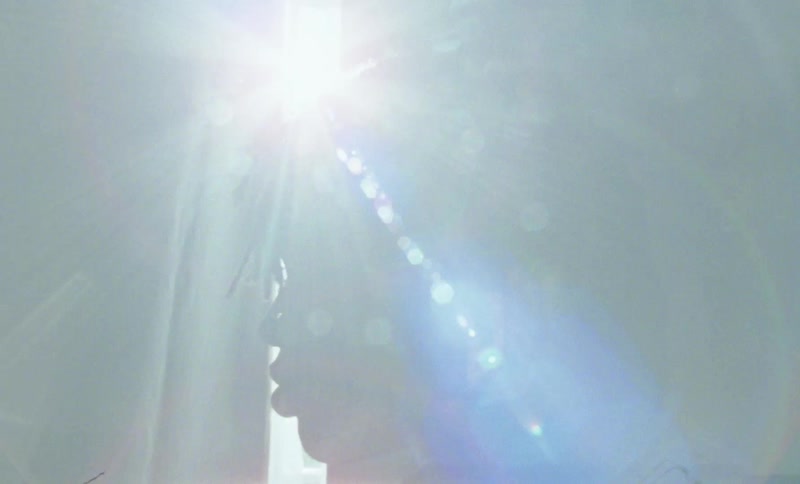 A young man looks out the window as the bright sun shines in on him