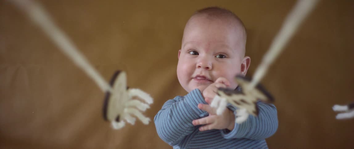 A baby lying on its back looks up at the mobiles hanging from strings above