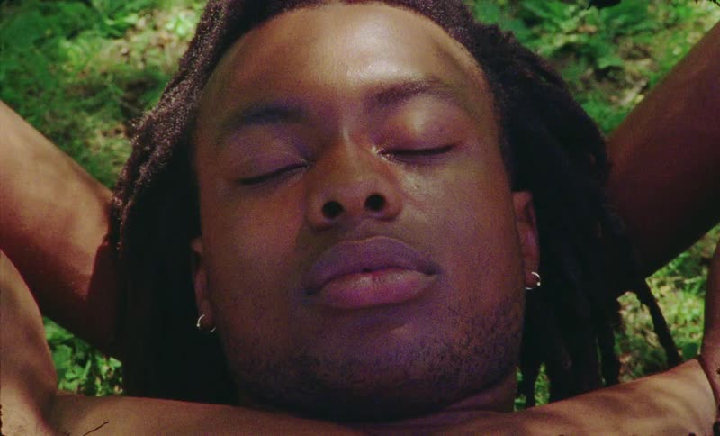 A black male lays on his back on the grass while resting in the shade