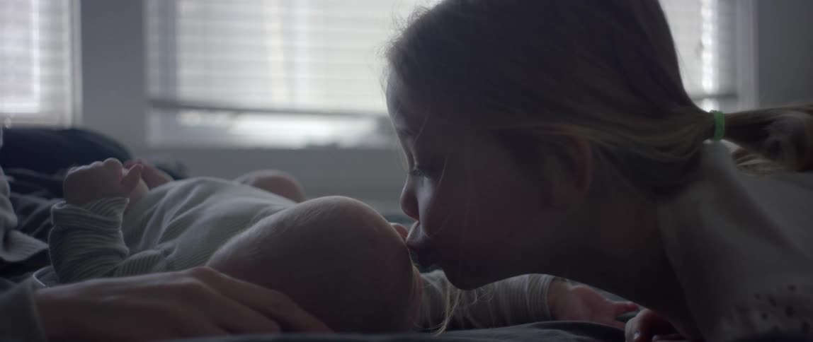 A little girl kisses her newborn sibling on a bed