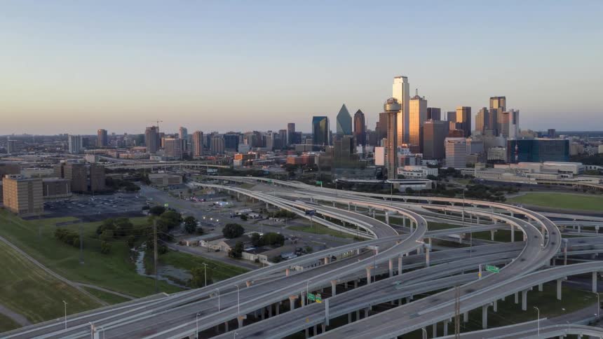 Time lapse aerial view of a city skyline with a large highway overpass in the evening