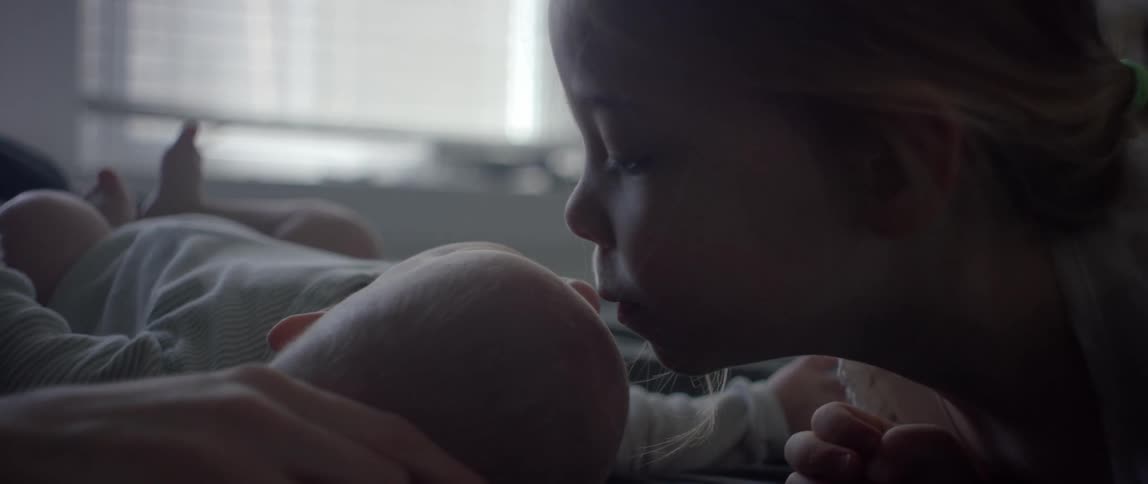 A little girl kisses her sibling lying on a bed indoors