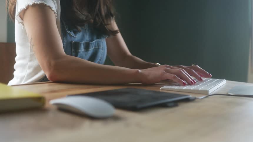 Woman typing on a white keyboard over a wooden table in a room