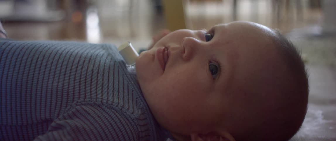 A baby lies on their back on a rug indoors smiling