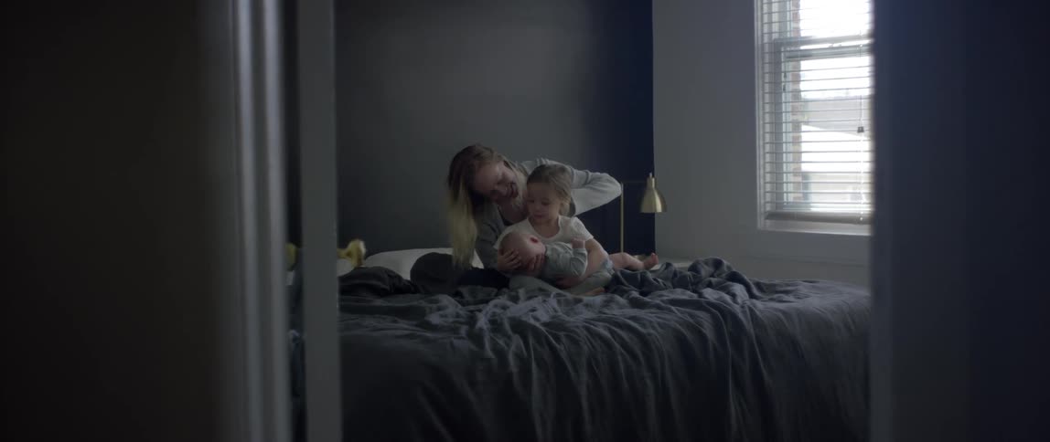 Mother lets daughter hold a baby while sitting in bed in the bedroom at home