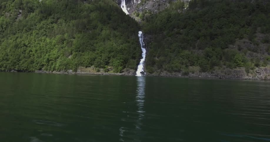 Waterfall flowing down a tree covered mountain into a body of water