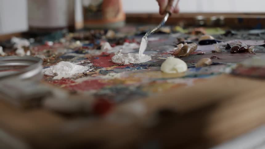 An artist uses a painter's knife to mix oil paint