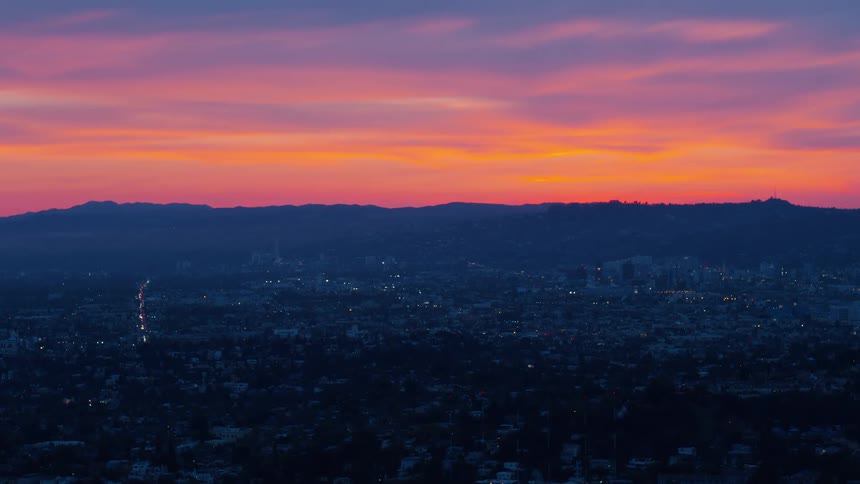 Silhouette of city and mountains on the horizon and colorful orange sky as sun has set