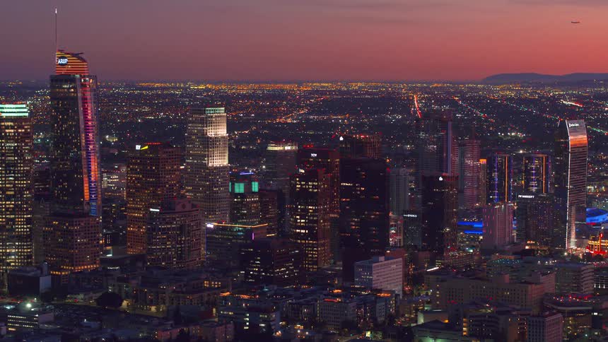 City and skyscraper lights shine as a plane moves across the sky