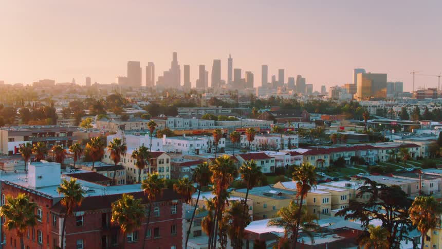 The camera travels towards downtown Los Angeles with a row of palm trees in the foreground