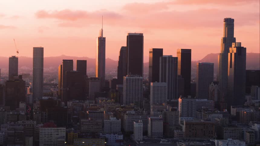 The sun is setting behind the large downtown Los Angeles skyline