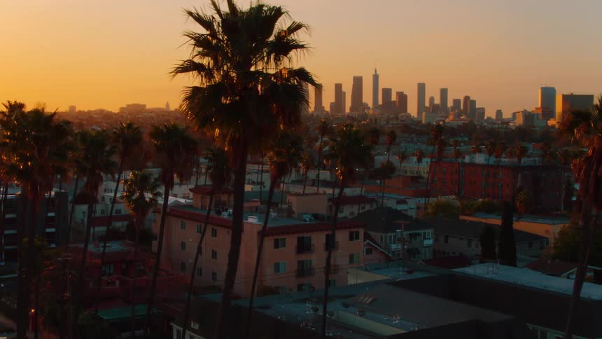 Skyscrapers loom in the distance of a city neighborhood covered in the orange light of the setting sun