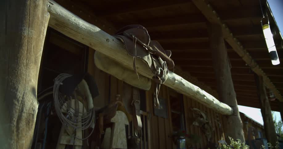 A saddle sits on the rail of a wooden building on a sunny day