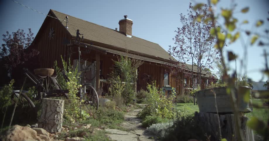 A stone path leads to a farmhouse with flowers and green garden