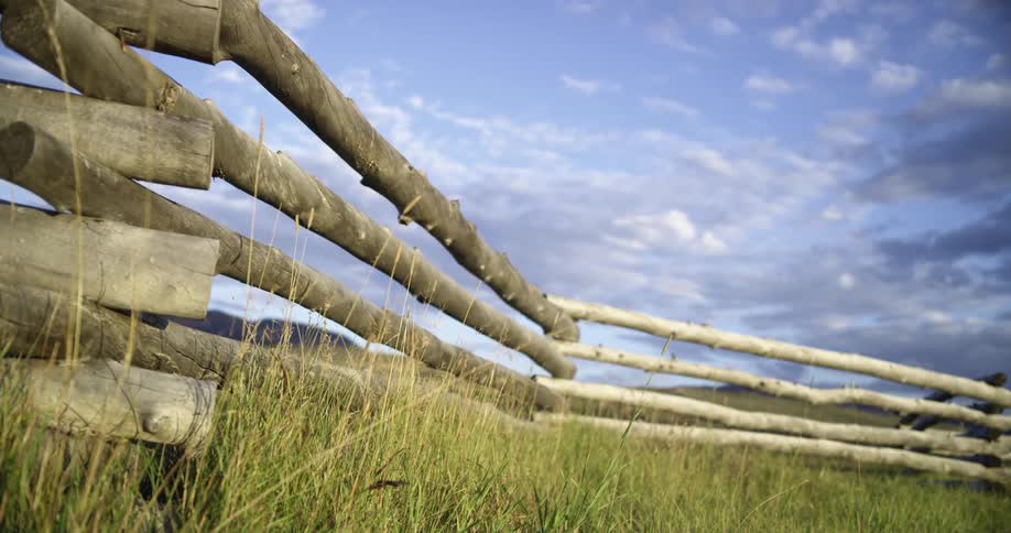 Wooden fence outdoors surrounding a field of grass at daytime in the countryside