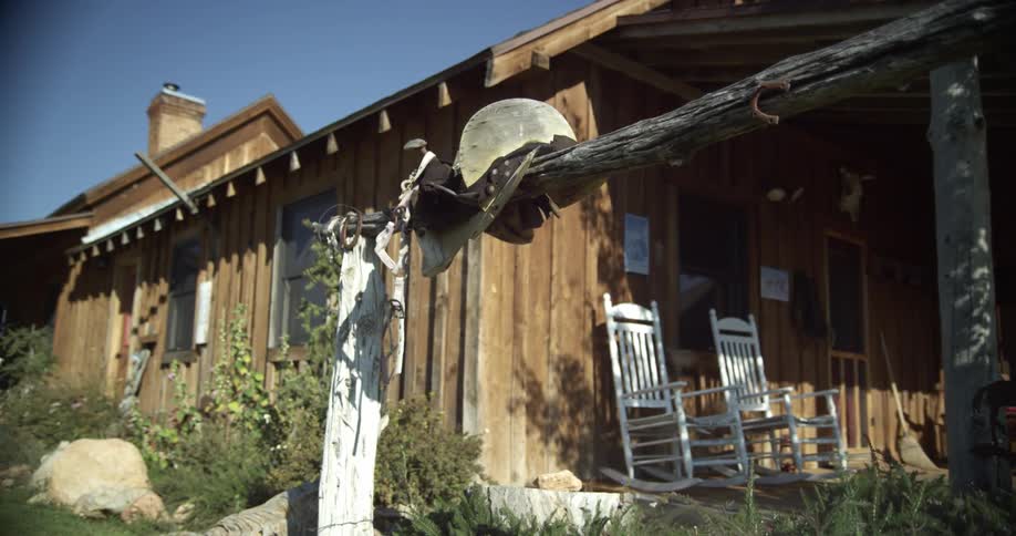A wood cabin with white rocking chairs on the front porch with blue skies