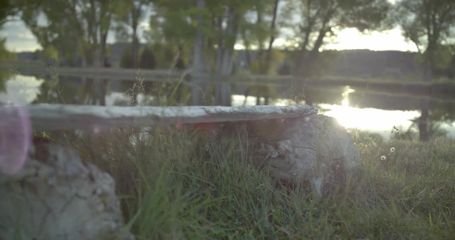 Rustic stone bench near a pond reflecting a low sun off of its pristine surface with trees in the background