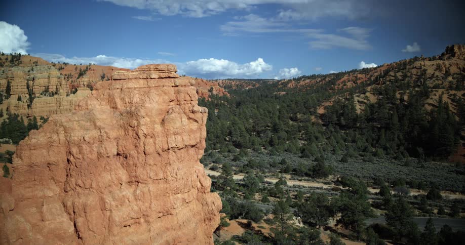 Canyon escarpment with valley below and mountains in the distance and clouds in the sky