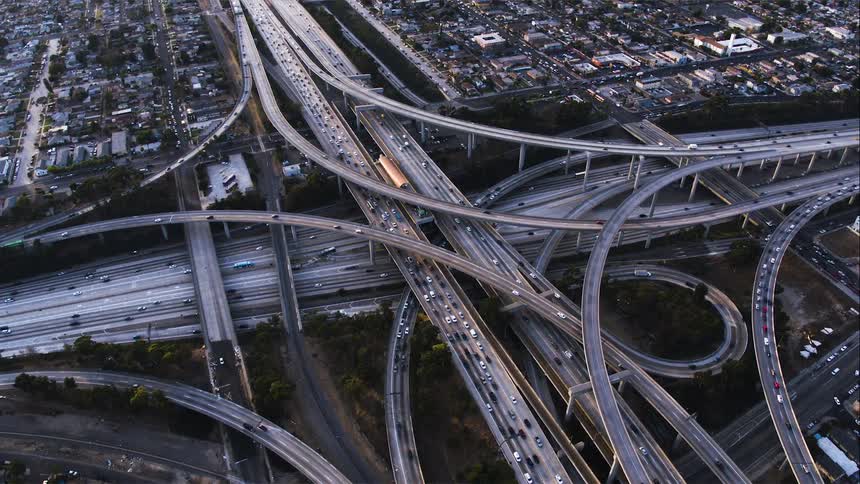The camera orbits above a swirling interchange of cars in Los Angeles at rush hour
