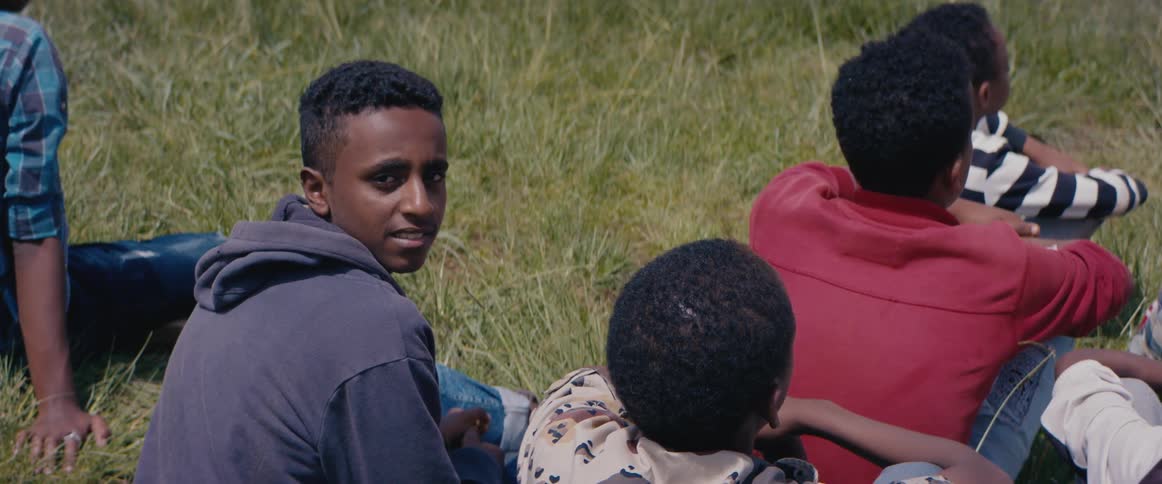 Young teenager sitting in the grass with friends turns around to look at the camera