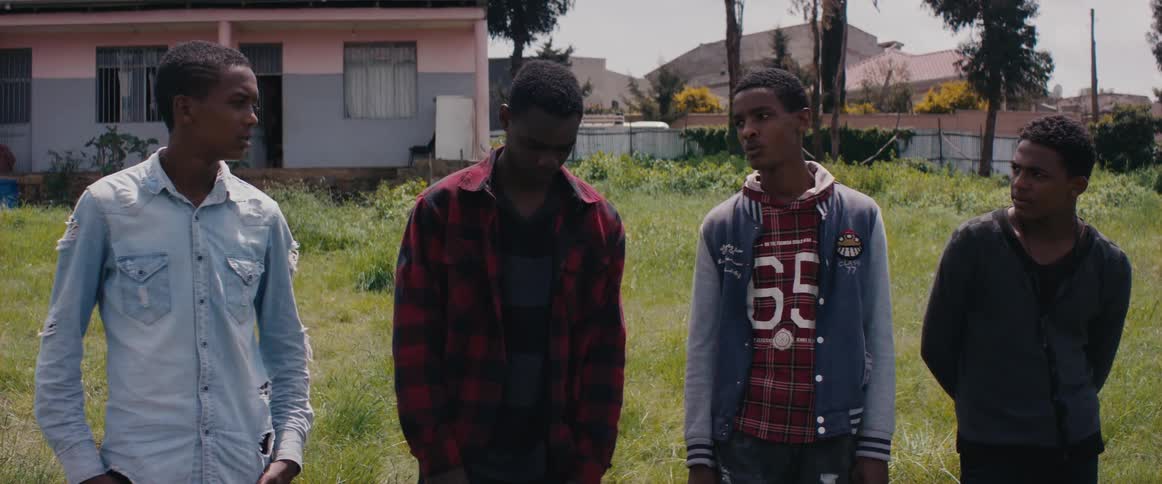 Four teens stand in a field in front of a house