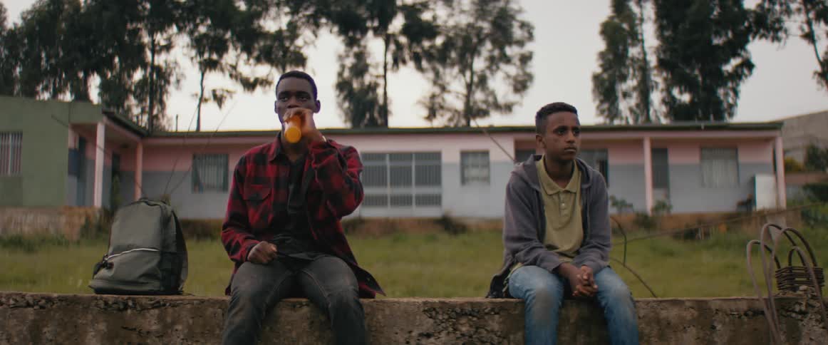 Two young teenagers sitting in front of the porch of a house share a carbonated drink in the evening