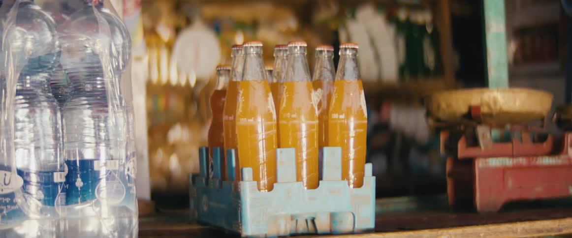 A store with glass bottles of orange liquid next to plastic water bottles on a wooden shelf