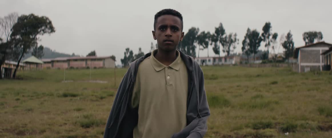 Boy runs down a slope in a field with houses in the distance at daytime