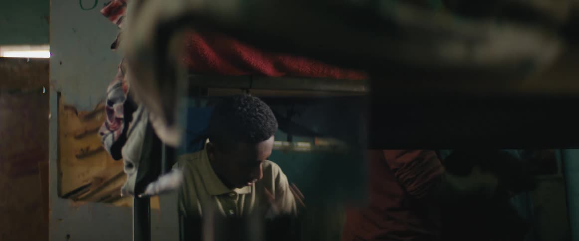 A boy buttons his shirt and rubs his shoulders as he gets ready in a bedroom with bunk beds