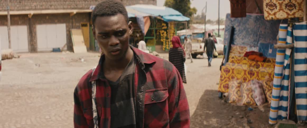 An upset young man walks slowly through a town before stopping to looking at something out of frame