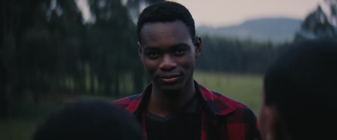 People jump around a man who stares down then looks up at the camera outdoors