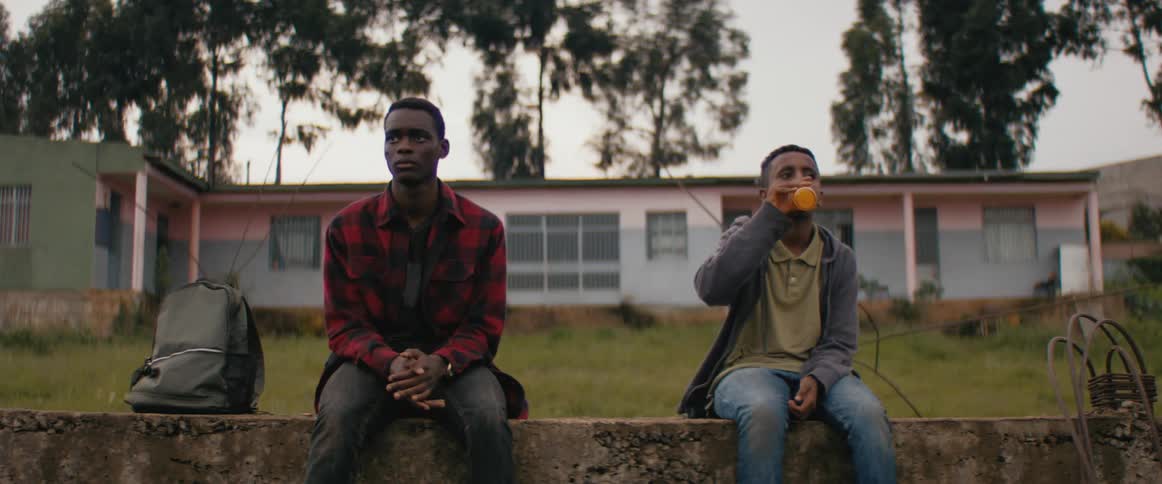Two teenagers sitting on a ledge in front of a house drinking carbonated soft drink at sunset