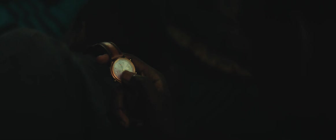 A man holds a wristwatch on his hand inside a very dark room