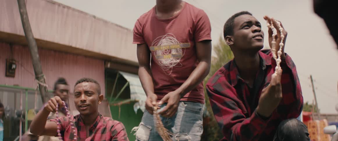 Three men crouch on the road in a developing city and shake necklaces for sale to passersby who do not stop