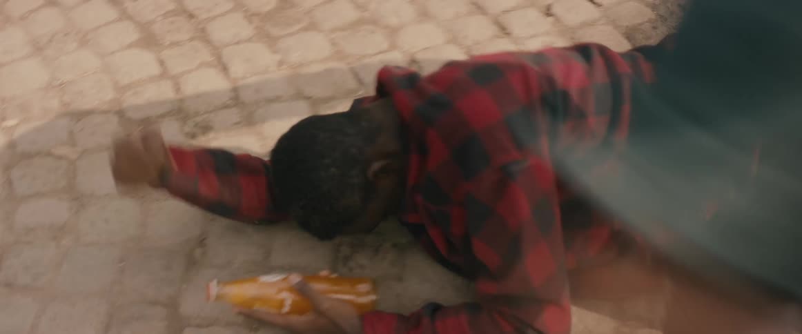 A man punches and kicks another man on the ground while holding an orange soda bottle