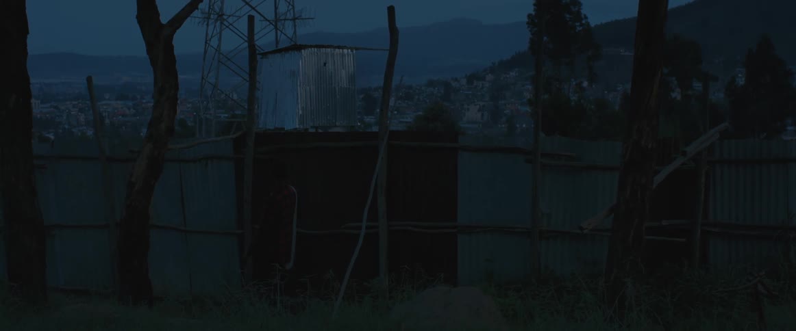 A man tries to climb over a tall fence that surrounds a neighborhood but falls and turns back around