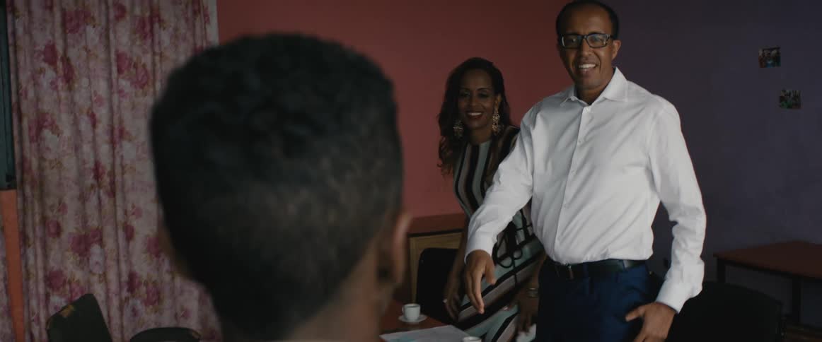 A man and woman sit in an office and then stand up when a woman and child walk in