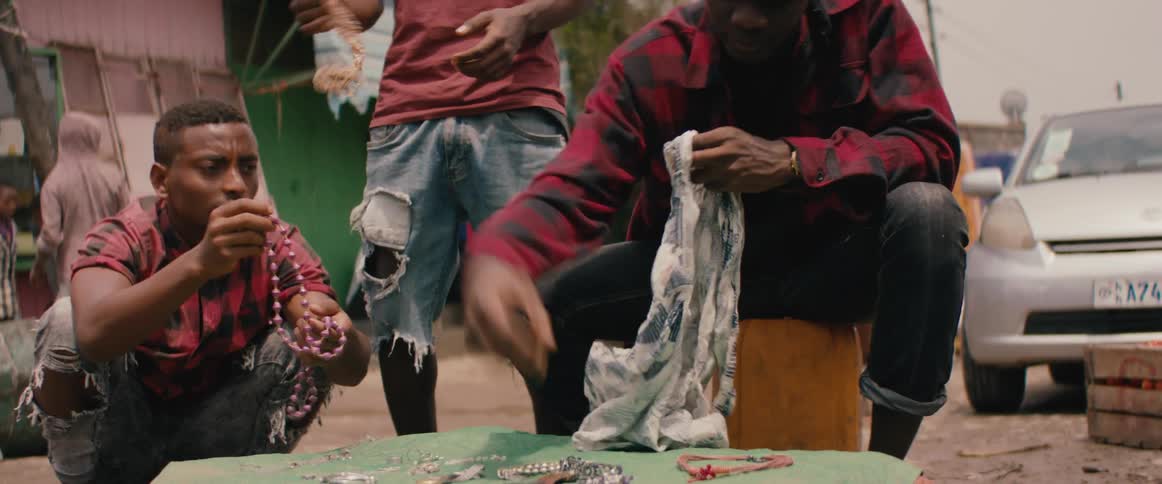 Men at a table covered with bead necklaces some shake them and one man puts them in a bag