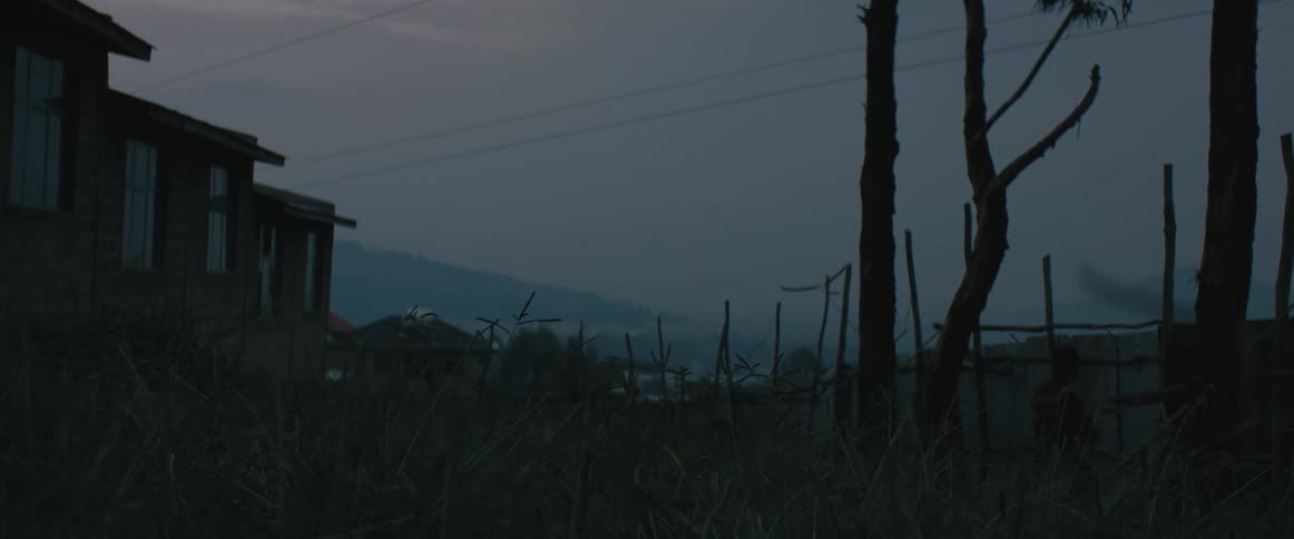 A person with a bag walking up to and climbing a fence with buildings the sky and clouds in the background