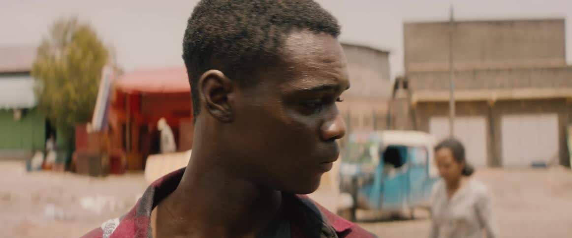 A man stands in an unpaved road near businesses and looks around before walking off