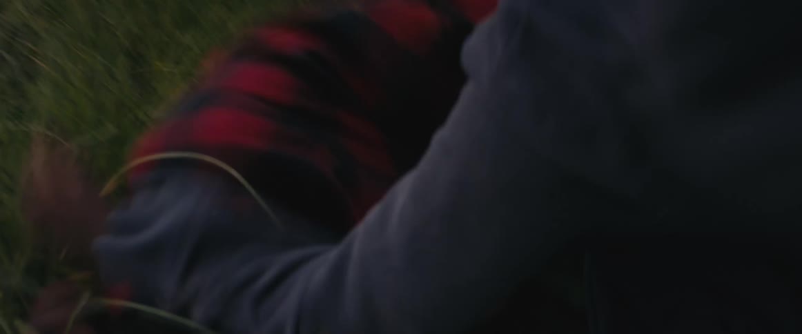 A teenage boy runs up a grassy hill to push down another person