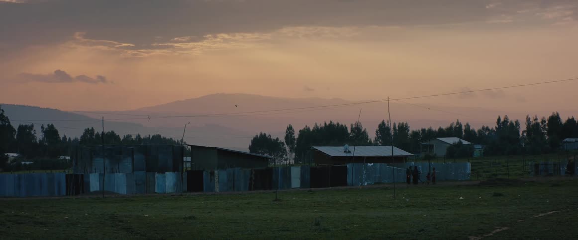 Small rudimentary houses surrounded by a makeshift fence in a grassland on a cloudy evening