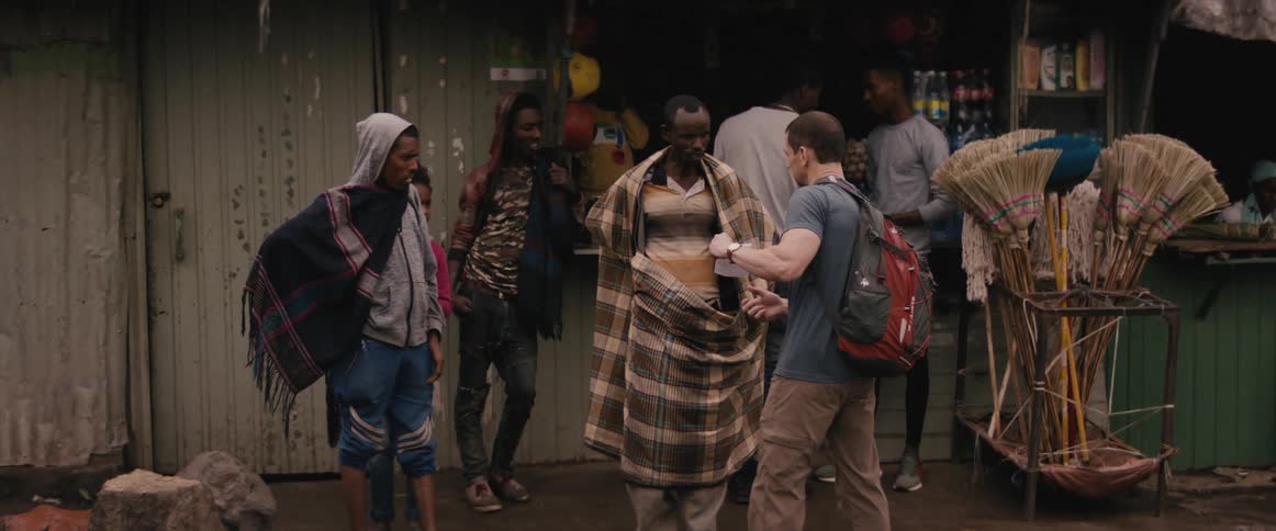 Men stand outside store while one man ask about a map while vans and trucks drive by