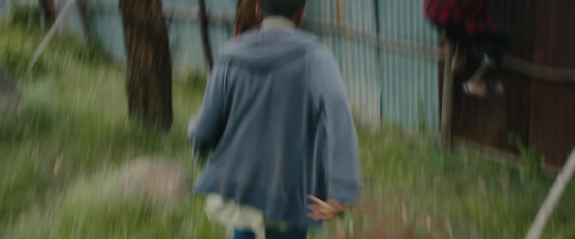 A young boy runs through a yard and pulls down a male teenager trying to climb a fence during the day