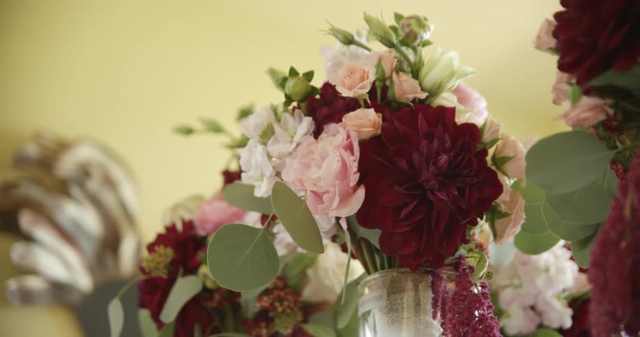 Arrangements of red pink and white flowers in a vase on a table indoors at daytime