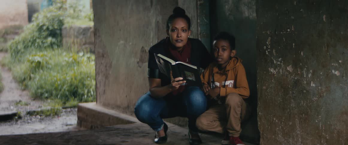 Mother and son pose near door with book near overgrown yard