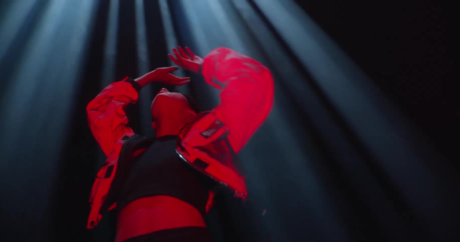 Woman wearing a crop top and a bomber jacket posing under rays of light in a dark room