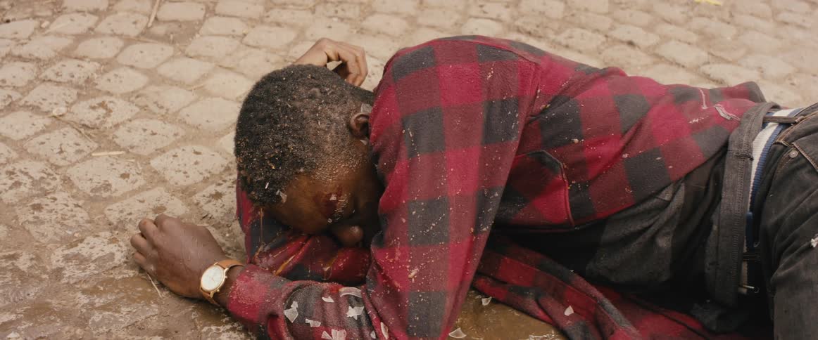 A black man is on the ground and is startled when something is thrown at him